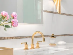 Elegant bathroom sink with gold faucet, black cabinetry, marble countertop, and pink flowers in a vase.