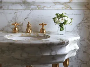 Elegant marble bathroom sink with gold fixtures and a small vase of white flowers on the countertop