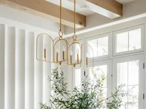 Bright modern dining room with wooden beams, white chairs, sculptural chandelier, and glass doors with greenery.