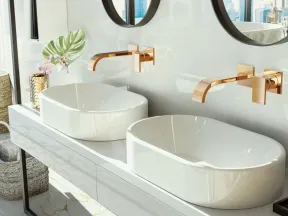 Modern bathroom with dual white vessel sinks, gold faucets, round mirrors, and decorative plants by a window.