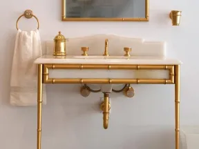 Elegant bathroom sink with gold metal frame, matching gold faucet fixtures, mirror, and towel holder.