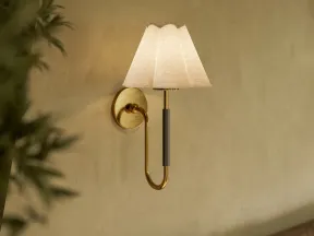 Elegant wall sconce with brass arm and white fabric shade mounted on a beige textured wall.