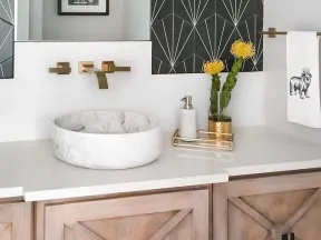 Modern bathroom vanity with a round marble sink, gold faucet, geometric black wall art, and wooden cabinets