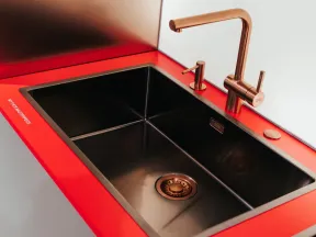 Modern black kitchen sink with copper faucet and soap dispenser set in vibrant red countertop.
