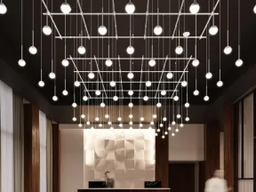 Modern office lobby with geometric wall design, hanging spherical lights, black curved sofas, and a wooden reception desk.