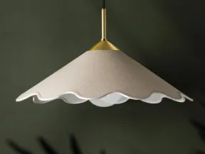 Modern pendant light with scalloped beige shade and brass fixture hanging against dark green wall.