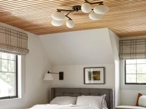 Cozy bedroom with wood slat ceiling, gray upholstered bed, neutral linens, striped rug, and natural light windows.
