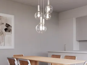 Modern dining room with wooden table, six cane chairs, minimalist pendant lights, and neutral artwork on wall