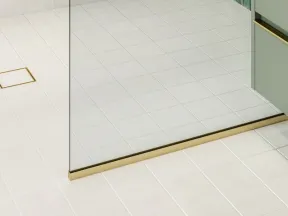 Modern bathroom shower with green tiled wall, gold fixtures, glass partition, and white tiled floor.