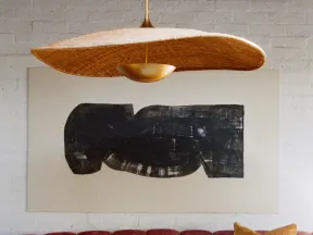 Curved red velvet sofa with mustard pillow under large abstract black art and woven pendant light.