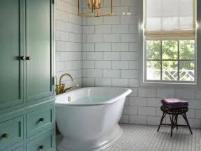 Elegant bathroom with white freestanding tub, green cabinet, hexagonal floor tiles, and gold chandelier under black ceiling.