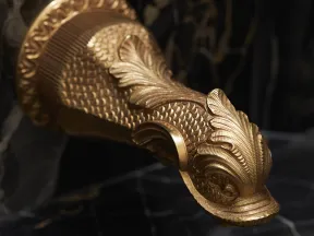 Ornate gold fish-shaped faucet on black marble with intricate scales and leaf designs in luxury bathroom.