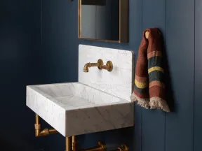 Modern bathroom with white marble sink, brass fixtures, arched mirror, navy blue walls, and striped hanging towel.