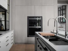 Modern kitchen with sleek white cabinets, built-in oven, black countertop, and dual curved faucets on island sink.