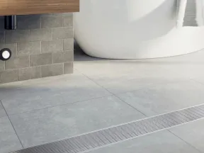 Modern bathroom with freestanding bathtub, gray tiles, wooden vanity, and metal floor drain cover.