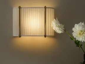Warm light from a striped wall sconce illuminates a decorative marble mantel with white flowers and a dark vase.