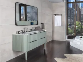 Modern bathroom with green vanity, large mirror, freestanding tub, dark wood floor, and city view through tall windows