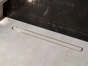 Modern linear gold shower drain set in a gray stone floor with dark marble wall background in a sleek bathroom.