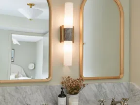 Modern bathroom vanity with marble countertop, double sinks, brass fixtures, arched mirrors, and wall sconce lighting.