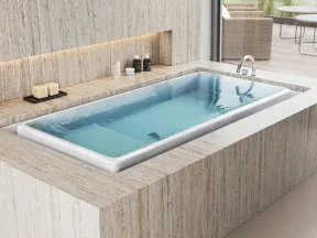 Modern bathroom with a rectangular built-in bathtub in beige stone and natural light from a large window.