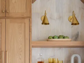 Wooden kitchen cabinets and shelves with gold accents, decorative items, and white marble countertop below.