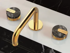 Modern gold faucet with black marble hot and cold knobs on a white countertop and black marble surroundings.