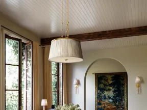 Elegant living space with large windows, vintage table and chair, floral centerpiece, and soft natural light.