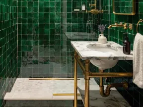 Modern bathroom with glossy green tiles, brass fixtures, marble countertop, and a glass-enclosed shower area.