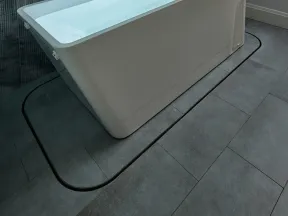 Modern rectangular white bathtub filled with water against a textured gray tiled wall and floor.