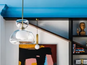 Modern pendant light hangs in front of abstract painting and bookshelf with decorative items in stylish room.