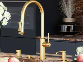 Modern kitchen sink with a gold faucet, marble countertop, and dark cabinetry accented by decorative plants.