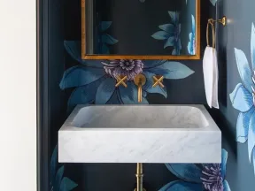 Elegant bathroom with floral dark wallpaper, gold fixtures, marble sink, and arched mirror framed in gold.
