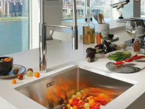 Modern kitchen sink with a chrome faucet, colorful tomatoes, eggplants, and city river view in the background