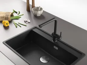 Modern black kitchen sink with matte black faucet on gray countertop with vegetables and kitchen tools nearby
