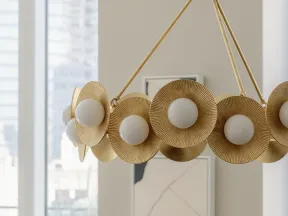 Modern gold chandelier with round white bulbs and textured circular accents in bright room.