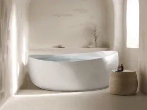 Modern white freestanding bathtub in a minimalist arched bathroom with natural light and woven side table.