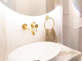 Modern bathroom sink with gold faucet and towel ring, illuminated white countertop and round mirror.