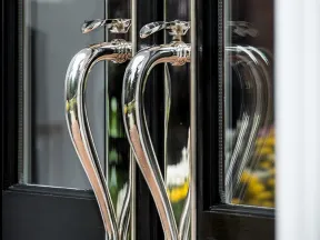 Close-up of shiny silver door handles on black-framed glass doors with reflections.