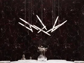 Modern dining room with round marble table, gray upholstered chairs, unique linear pendant lights, and dark marble wall.