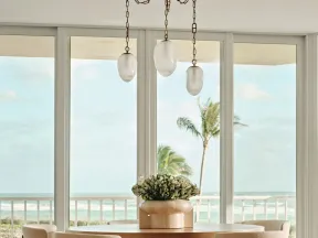 Modern dining area with wooden table, cozy chairs, pendant lights, and ocean view through large windows.