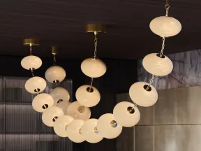 Modern chandelier with round, glowing white globes linked by gold chains in a stylish interior space.