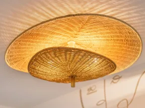 Woven rattan ceiling light casting patterned shadows on white ceiling with abstract face wall art.