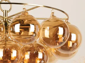 Modern chandelier with amber glass globe lights hanging from a gold metal frame against a neutral background.