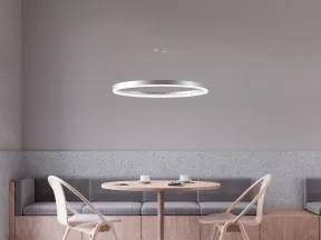 Minimalist dining area with round wooden table, two wooden chairs with cushions, bench seating, and circular pendant light.