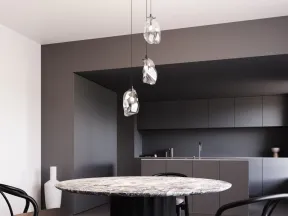 Modern dining space with round marble table, black chairs, and three pendant lights in a minimalist kitchen.