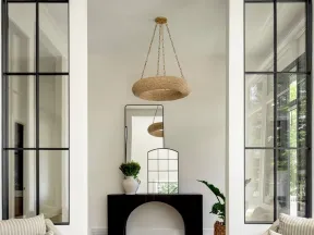 Bright living space with striped armchairs, black console table, mirrors, plants, and woven ceiling light.
