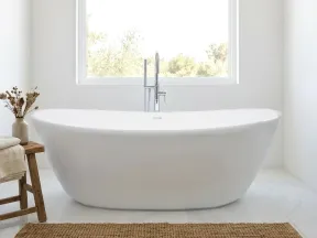 Modern white freestanding bathtub in a bright minimalist bathroom with a large window and natural decor.