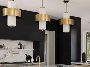 Modern kitchen with black walls, marble island, gold fixtures, and black velvet chairs under brass pendant lights.