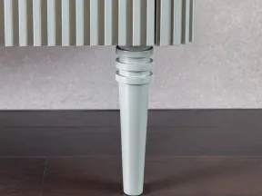 Close-up of a white wooden tapered leg supporting a piece of ribbed furniture on dark hardwood flooring.