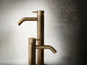 Two textured bronze faucets with a woven pattern and sleek spouts against a textured neutral background.